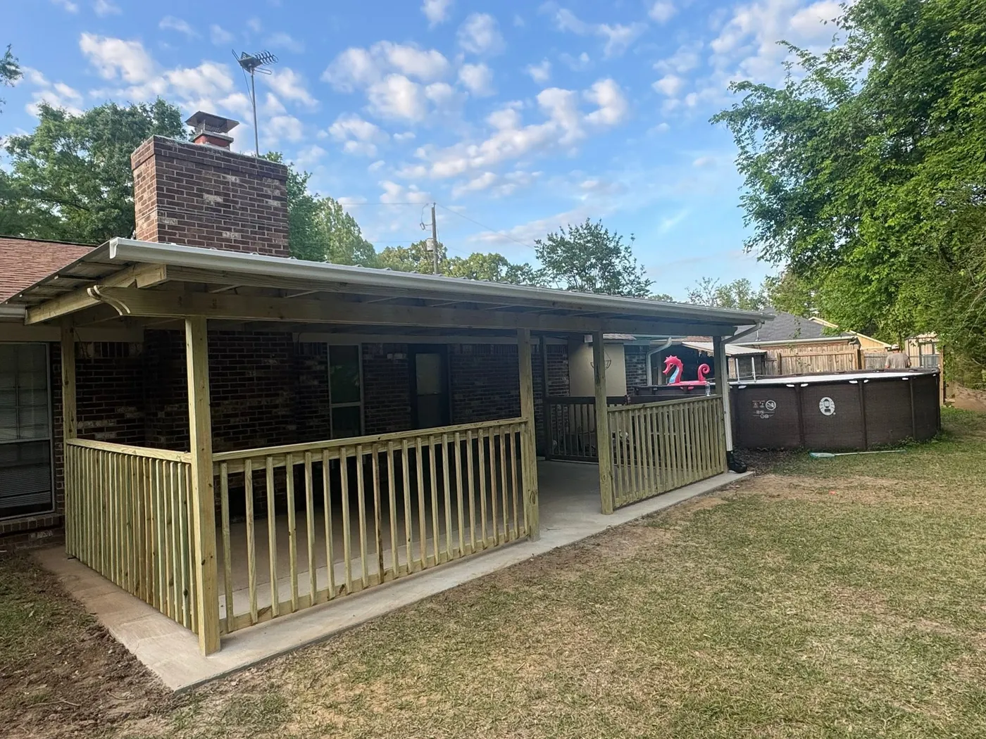 Covered back porch with a wood railing and a brick chimney beside it