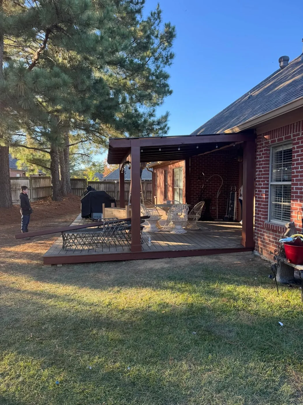New stained pergola over a deck beside a brick house