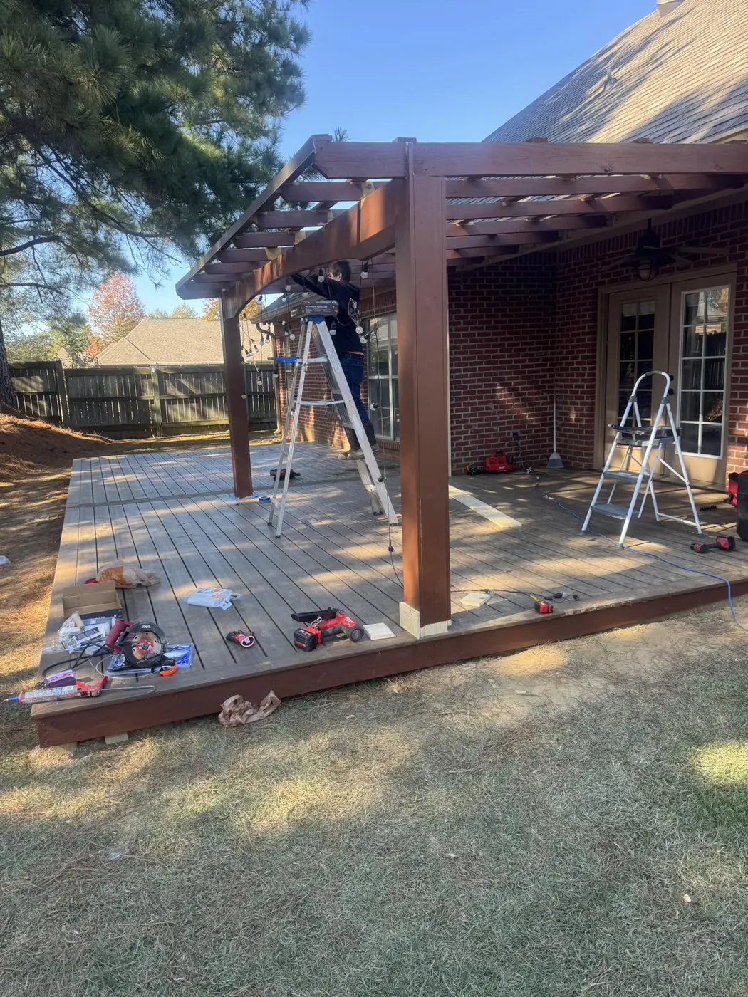 Stained pergola and deck under construction with tools and ladders on the boards