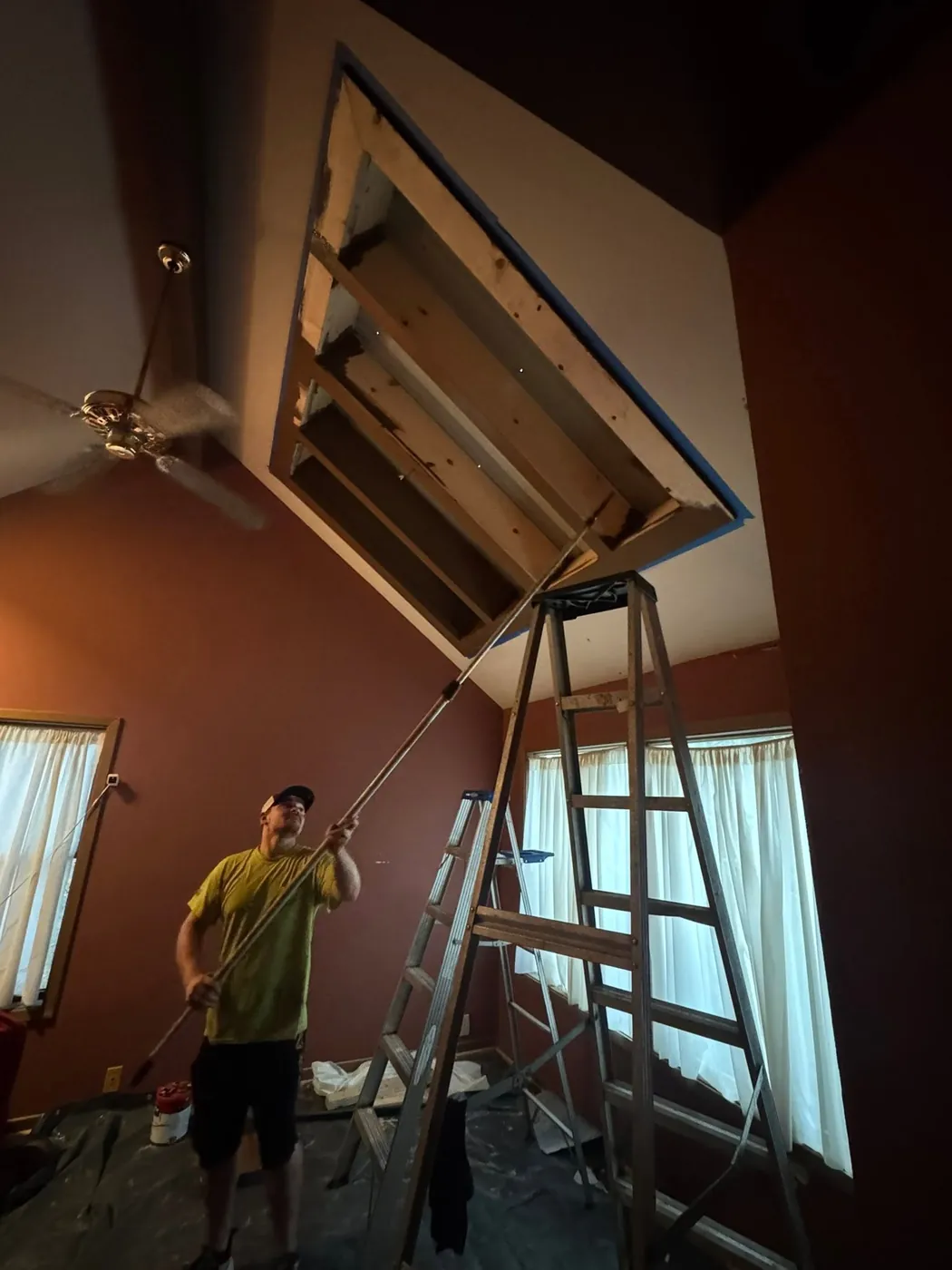 Crew member on a ladder working at a framed ceiling opening in a tall room