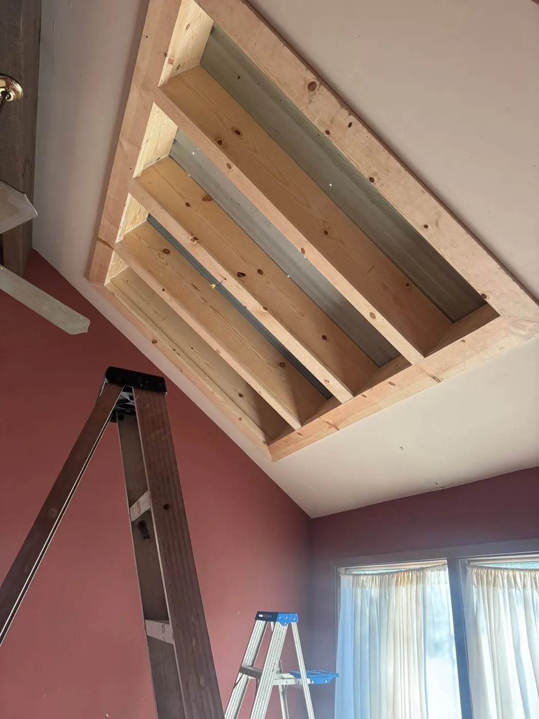 New wood framing inside a high ceiling above a painted wall
